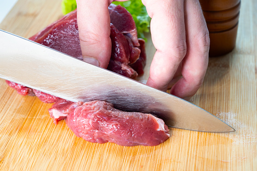 Cropped shot of a man slicing a prepared piece of meat in a commercial kitchen