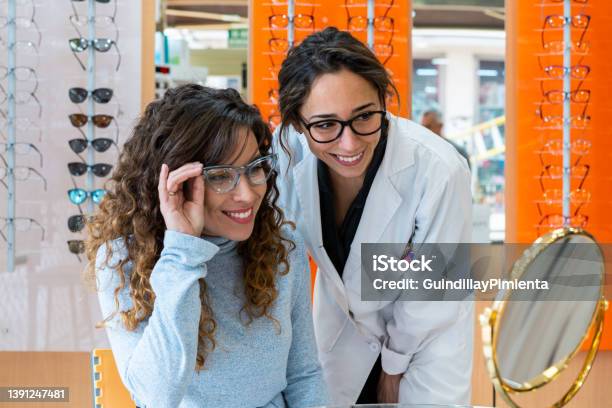Happy Female Optician And Client Wearing Glasses And Looking At The Mirror Stock Photo - Download Image Now