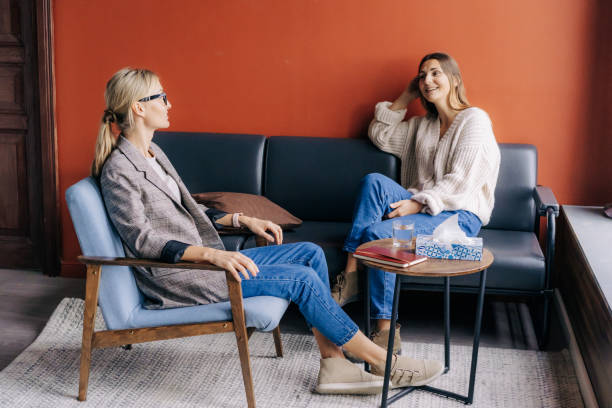 smiling female client sitting on the couch talking to a female psychotherapist in a stylish office. - color image bus discussion expertise imagens e fotografias de stock