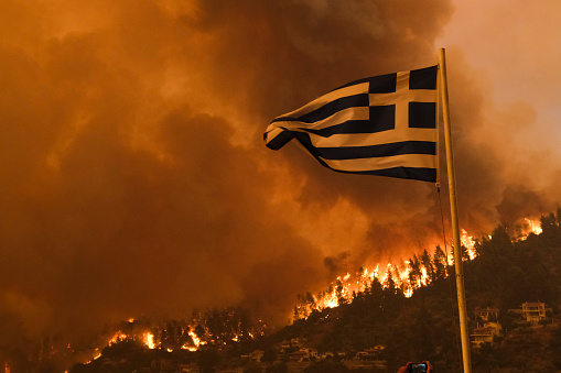 A Greek flag waves on a hill as flames approaching at the village of Gouves, on the island of Evia in Greece on August 8, 2021.
