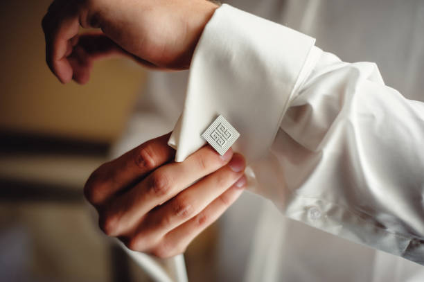 A successful man wears silver cufflinks on the cuff of a white shirt. The hands of the bridegroom fix a cufflinks on the sleeve of a white shirt. Close-up Men's accessories. Morning of the groom A successful man wears silver cufflinks on the cuff of a white shirt. The hands of the bridegroom fix a cufflinks on the sleeve of a white shirt. Close-up Men's accessories. Morning of the groom cufflink stock pictures, royalty-free photos & images