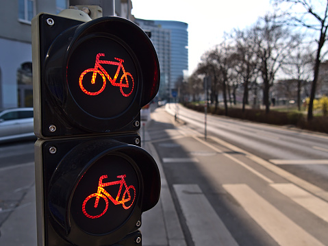 Close-up view of red traffic light for bicycles on cycling path next to a road in the downtown of Vienna, Austria on sunny day. Focus on the two traffic lights with bokeh background.