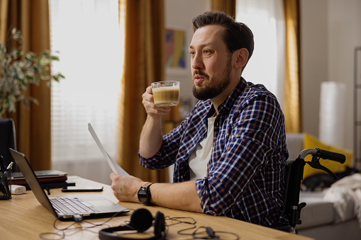 A happy middle-aged man takes a break from work to drink coffee and talk to his roommate. An adult guy is working from home on an assigned case for a new client.