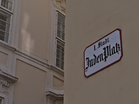 Close-up view of street sign on the facade of an old building in the center of the downtown of Vienna, Austria. Text on sign (German): Jewish Square (name of the location) and district.