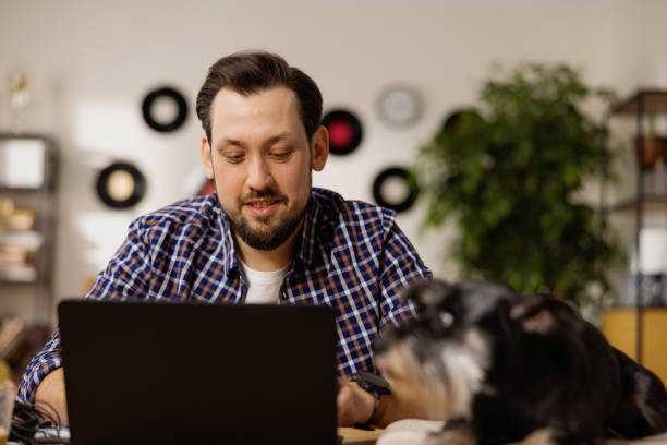 istock A handsome man works alone at home, filling out applications needed for work. A brunet is using a laptop, with a dog lying next to him. The man at the laptop. Working at home 1391251637