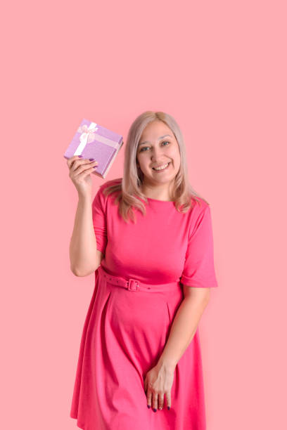40歳の金髪の女性は、ピンクの背景に立って彼女の手にギフトボックスを持っています - 35 40 years women female smiling ストックフォトと画像