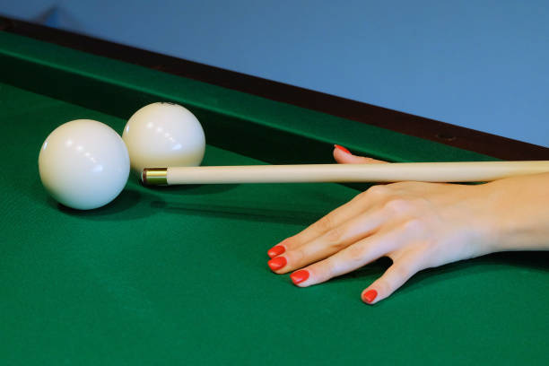 Woman playing billiard. Woman hand holds a cue for striking the white billiard ball. Selective focus on balls and cue tip. stock photo