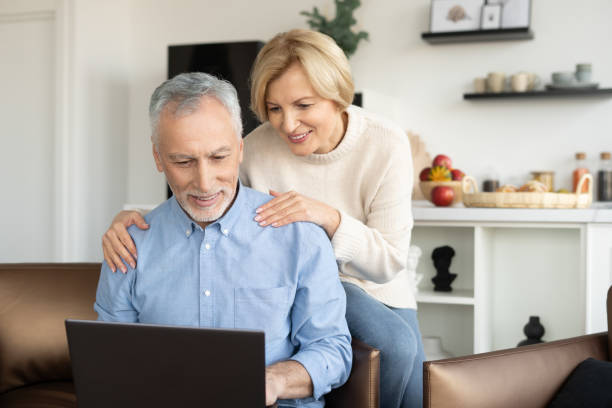 mature family couple watching video on laptop - senior adult happiness computer looking at camera imagens e fotografias de stock