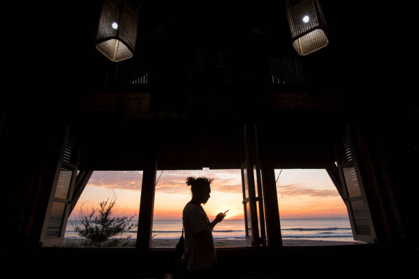 Silhouette Man Standing in Front of Window Using Phone at Sunset