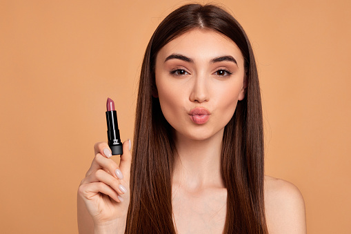 beautiful young girl using trendy nude pink lipstick isolated on beige background