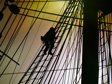 An anonymous silhouetted person ascending the rigging on the Cutty Sark sailing ship in Greenwich, London. (Colour manipulation.)