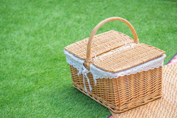 Vintage light brown wicker basket with mat on artificial green grass for picnic and recreation time stock photo