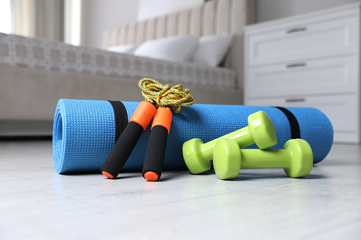 Dumbbells, skipping rope and yoga mat on floor indoors. Fitness at home