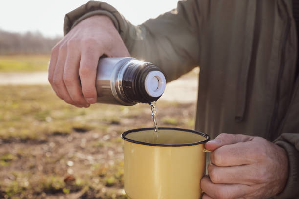 istock Man pouring hot drink into mug from thermos outdoors, closeup 1391274658