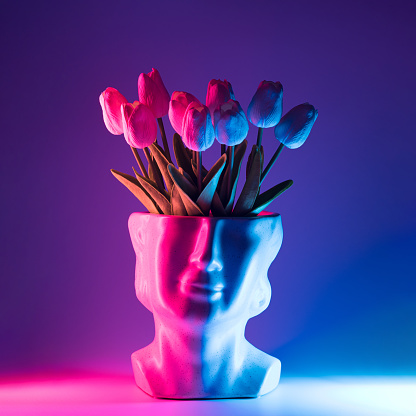 Head shaped flowerpot with tulips inside and neon led lights. Retro wave spring summer background.