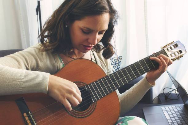 istock Attractive young lady playing and recording music using a Spanish classical guitar and a laptop 1391279304