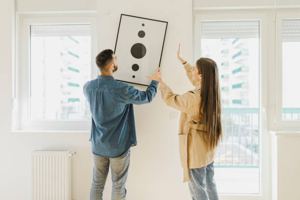 jeune couple aménageant un nouvel appartement, accrochant de la peinture, nouvelle maison et concept de déménagement. - home decorating photos photos et images de collection