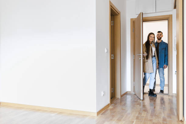 giovane coppia eccitata che apre la porta d'ingresso della nuova casa, la coppia che apre la porta e cammina nel salotto vuoto della nuova casa, la passeggiata completa della loro nuova casa - newly completed foto e immagini stock