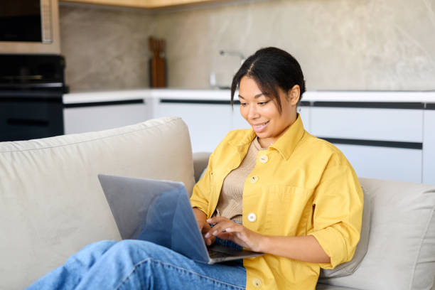 istock Young multiracial beautiful woman using laptop at home lying down on the couch 1391287474