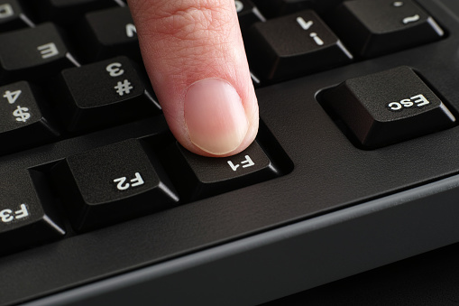 A finger pushing the F1 key on a black computer keyboard. Close up.
