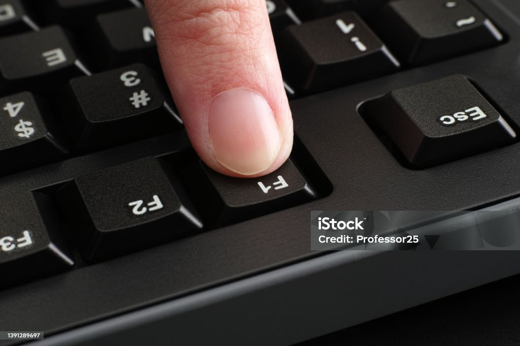 A finger pushing the F1 key on a black computer keyboard A finger pushing the F1 key on a black computer keyboard. Close up. Computer Keyboard Stock Photo