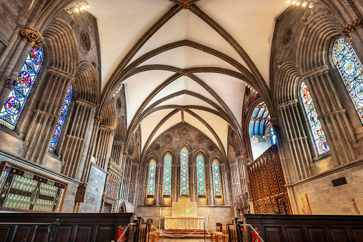 Inside the beautiful,ornate Cathedral church of the Anglican Diocese of Hereford,with Normon detailed architecture,distinctive lighting,illuminated altar,pews and stained glass windows.