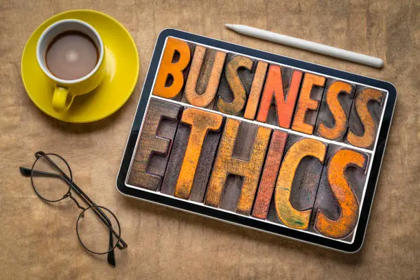 business ethics - word abstract in vintage letterpress wood type printing blocks on a digital tablet, flat lay with a cup of coffee