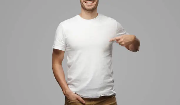 Photo of Young man pointing to his blank white tshirt with index finger, showing empty space