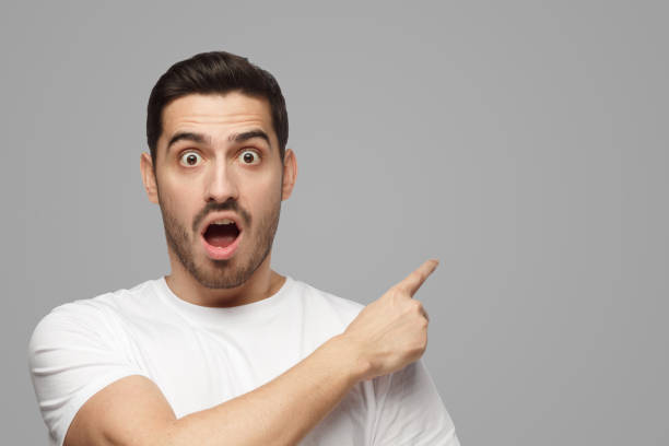 istock Young man looking at camera with mouth and eyes open with surprise, pointing right 1391298413