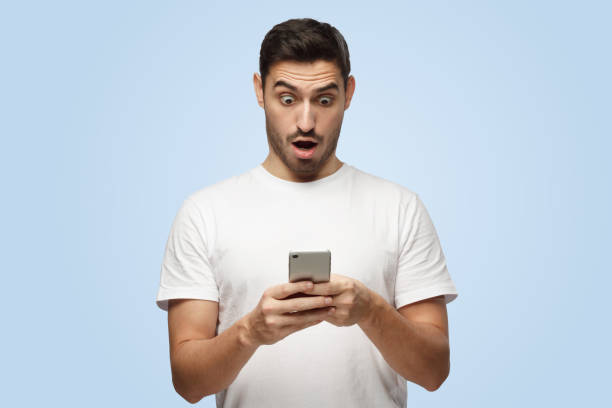 istock Attractive handsome young man holds smartphone looking scared and confused 1391298500