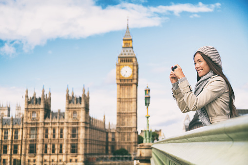 Travel tourist in london sightseeing taking photo pictures near Big Ben. Woman holding smart phone camera smiling happy near Palace of Westminster, Westminster Bridge, London, England.