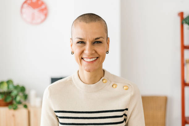 young successful business woman looking at camera from home office - kaal geschoren hoofd stockfoto's en -beelden