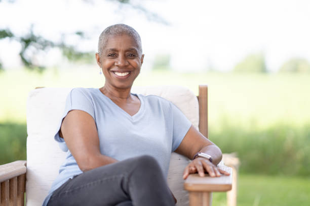 Portrait of a Woman Beating Cancer A middle aged woman of African decent, who is beating Cancer, is sitting outside on a sunny summer day as she poses for a portrait.  She is dressed casually in a light blue t-shirt and is smiling with the news that she is beating Cancer. food chain stock pictures, royalty-free photos & images
