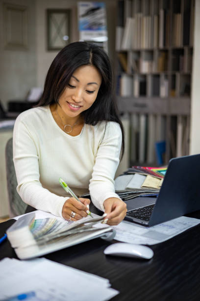 portrait of beautiful brunette woman interior designer working use laptop creating kitchen project - home decorating fabric swatch color swatch blueprint imagens e fotografias de stock