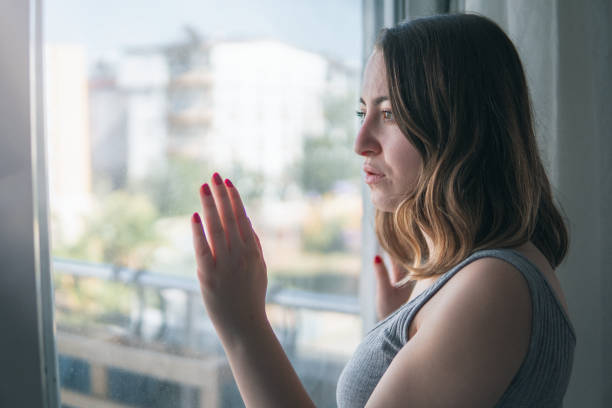 istock Sad young woman standing over window 1391307811