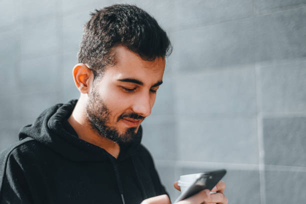 istock Young man using his smartphone and drinking coffee while walking in the city 1391307853
