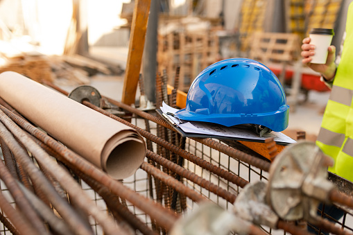 Manual worker's equipment at construction site without people. Blue safety helmet. Blueprints. Paperwork.