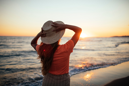 A woman in a hat enjoys the sunset at the beach