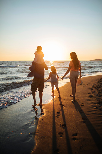 Happy family strolls along the beach at sunset