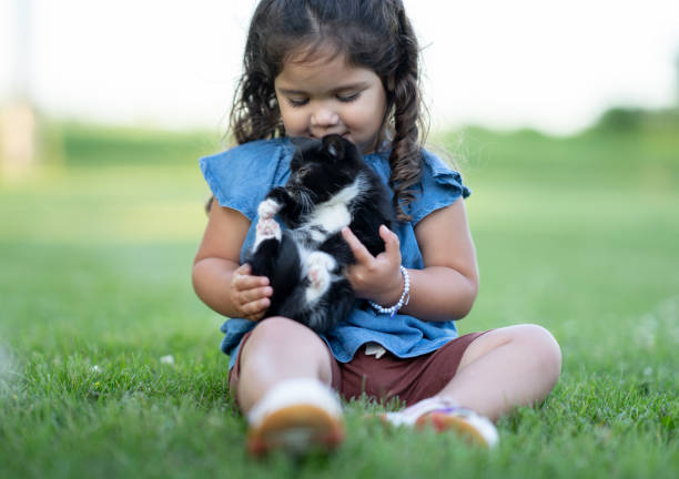 A blonde girl in a plaid dress plays with a red kitten in the garden