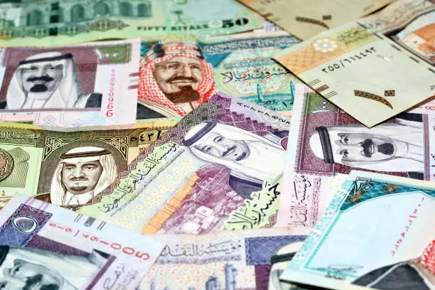 Background of a pile of Saudi Arabia riyals banknotes money bills of different values from different times, selective focus of a stack of Saudi riyals, kingdom of Saudi Arabia economy concept