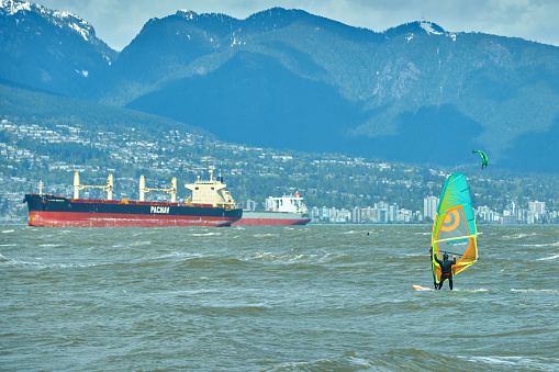 A wind surfer and kite surfers on English Bay on a windy day. Vancouver, British Columbia, Canada. April 27, 2019.