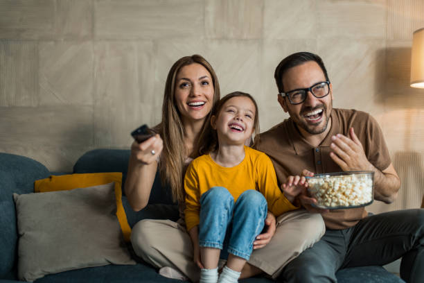Happy young family watching tv together at home. Two parents watching a movie with their little daughter at home. watching tv stock pictures, royalty-free photos & images