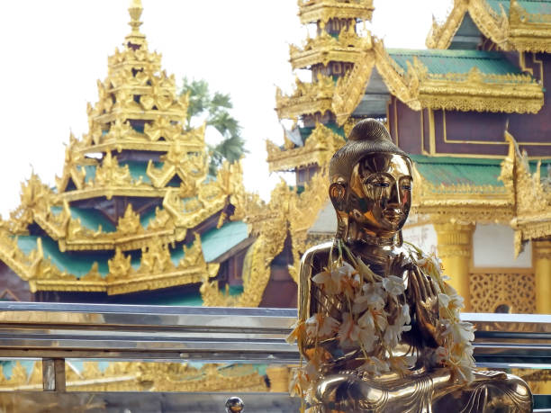 Yangon, Myanmar - August 1st, 2015: A gold sitting Buddha statue is adorned with flower garlands inside the grounds of Shwedagon Pagoda, a famous Buddhist temple