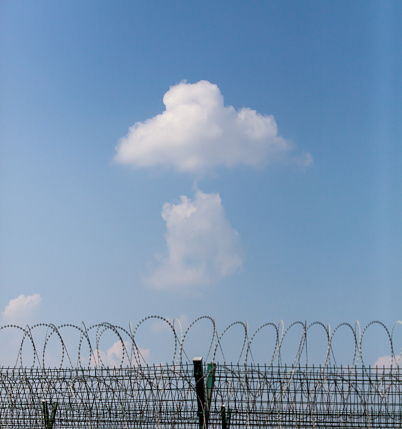 Iron fence and barbed wire wrapped around blue sky with textured clouds