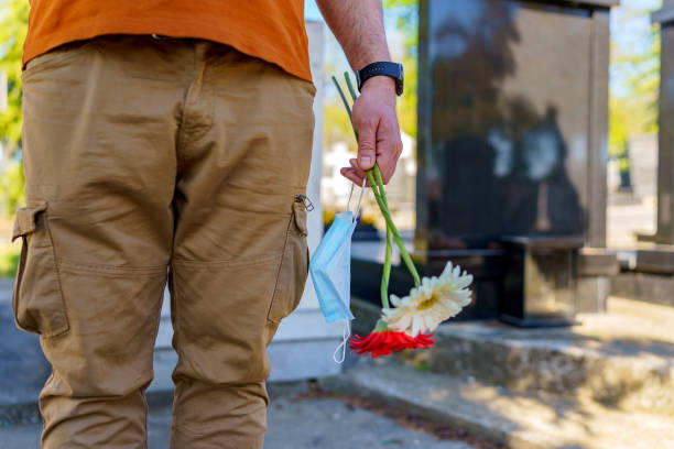 istock Man Placing Flowers By Headstone In Cemetery 1391355970