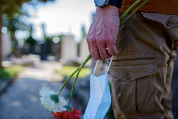 istock Man Placing Flowers By Headstone In Cemetery 1391355973
