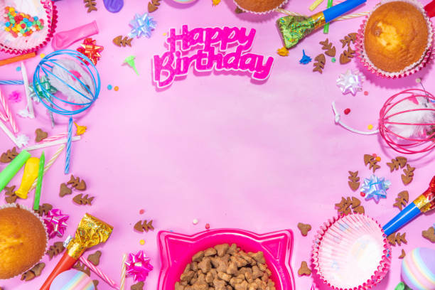 Pet cat happy birthday background with set different cats and kitty snack, food and toys, cat muzzle shape bowl, birthday cupcakes with happy birthday candles, accessories. Flatlay on pink background