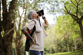 senior woman using binoculars to spot animals and things while hiking with backpacks and trekking in the forest. Concept of active lifestyle on retirement.
