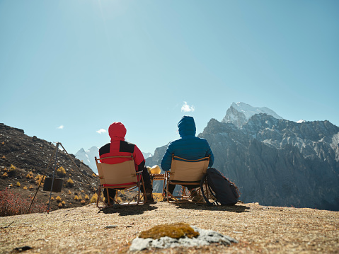 rear view of asian couple sitting in chairs on top of mountain looking at view in yading national park, daocheng county, sichuan province, china